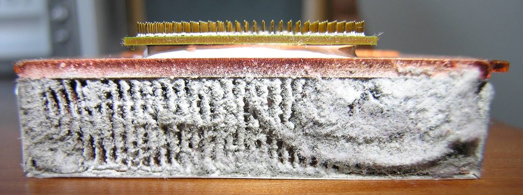 The copper base and fins of a laptop heatsink completely packed with a thick felt of grey dust and lint, seen from the side